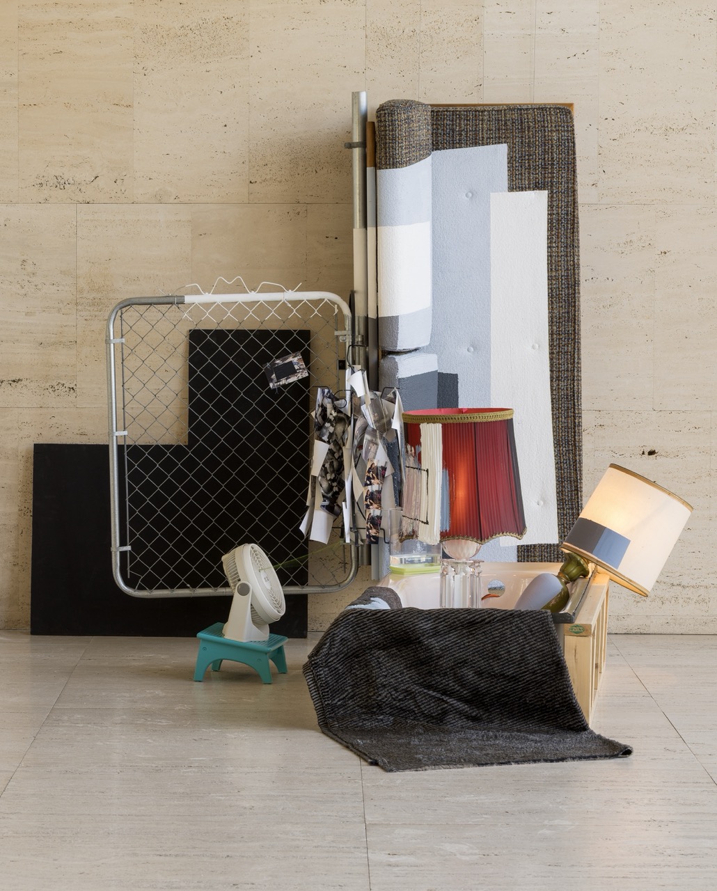 Abstract composition of furniture, fabric, lamps, and decor items against a stone wall.